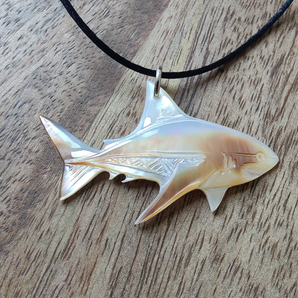 Pendentif requin en nacre gravée de Tahiti. Bijou polynésien aux reflets irisés, monté sur un lien noir ajustable.