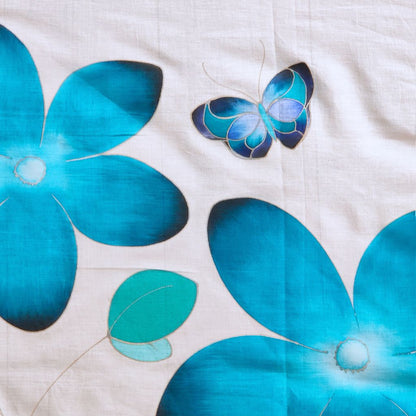 Détails du paréo tahitien en voile de coton, peint à la main à Tahiti, motifs fleurs de tiaré turquoise et papillon sur fond blanc. Paréo artisanal traditionnel
