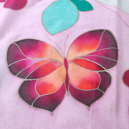 zoom sur le papillon du paréo tahitien en voile de coton, peint à la main à Tahiti, motifs fleurs de tiaré rose et papillon sur fond blanc et rose pastel. Paréo artisanal traditionnel