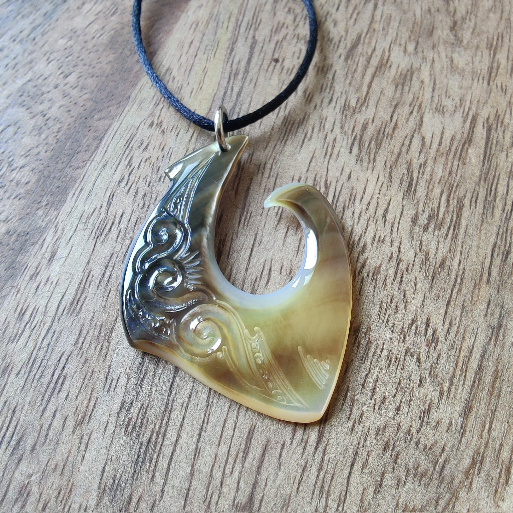 Pendentif hameçon en nacre de Tahiti, monté sur un cordon noir ajustable. Bijou polynésien authentique.