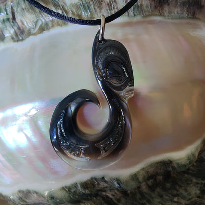 Pendentif  polynésien en forme d'hameçon avec visage Tiki, sculpté dans une nacre de Tahiti aux reflets sombres et irisés