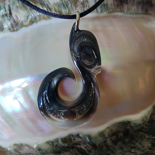 Pendentif  polynésien en forme d'hameçon avec visage Tiki, sculpté dans une nacre de Tahiti aux reflets sombres et irisés