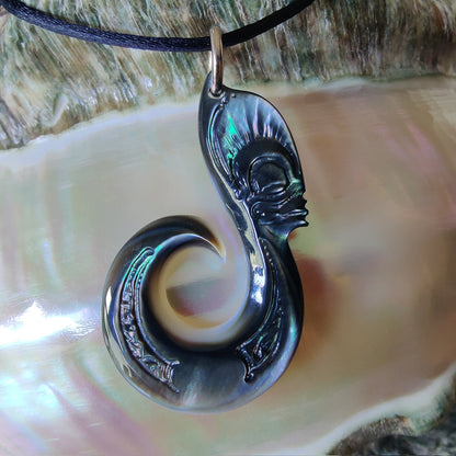 Pendentif  polynésien en forme d'hameçon avec visage Tiki, sculpté dans une nacre de Tahiti aux reflets sombres et irisés