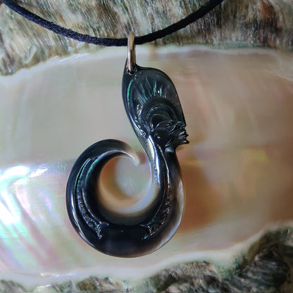 Pendentif  polynésien en forme d'hameçon avec visage Tiki, sculpté dans une nacre de Tahiti aux reflets sombres et irisés