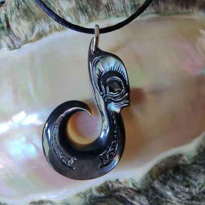 Pendentif  polynésien en forme d'hameçon avec visage Tiki, sculpté dans une nacre de Tahiti aux reflets sombres et irisés