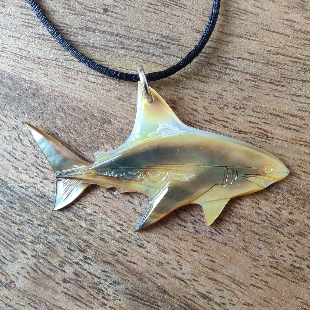 Pendentif requin en nacre gravée de Tahiti. Bijou polynésien aux reflets irisés, monté sur un lien noir ajustable.