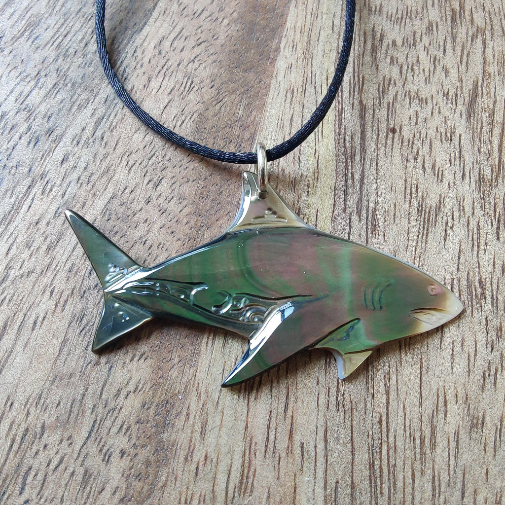 Pendentif requin en nacre gravée de Tahiti. Bijou polynésien aux reflets irisés, monté sur un lien noir ajustable.