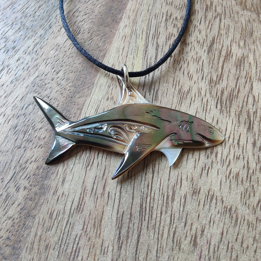 Pendentif requin en nacre gravée de Tahiti. Bijou polynésien aux reflets irisés, monté sur un lien noir ajustable.