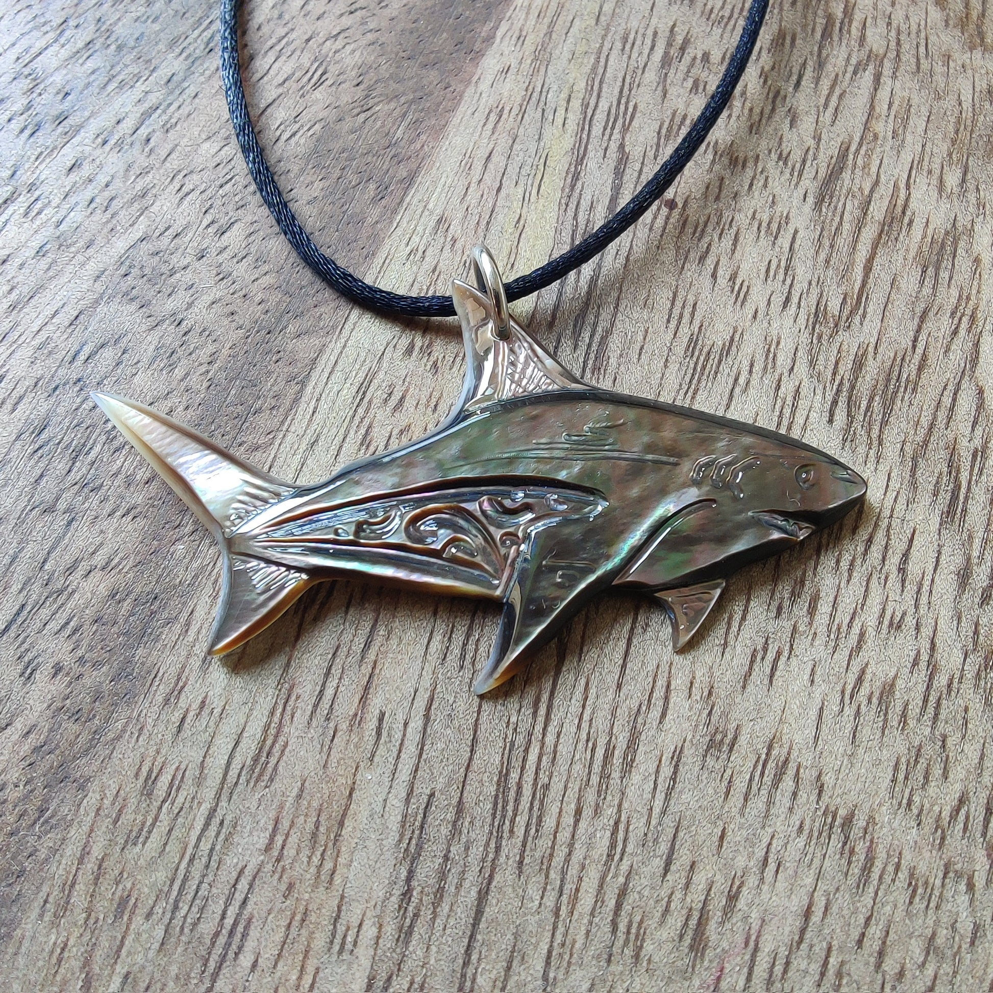 Pendentif requin en nacre gravée de Tahiti. Bijou polynésien aux reflets irisés, monté sur un lien noir ajustable.