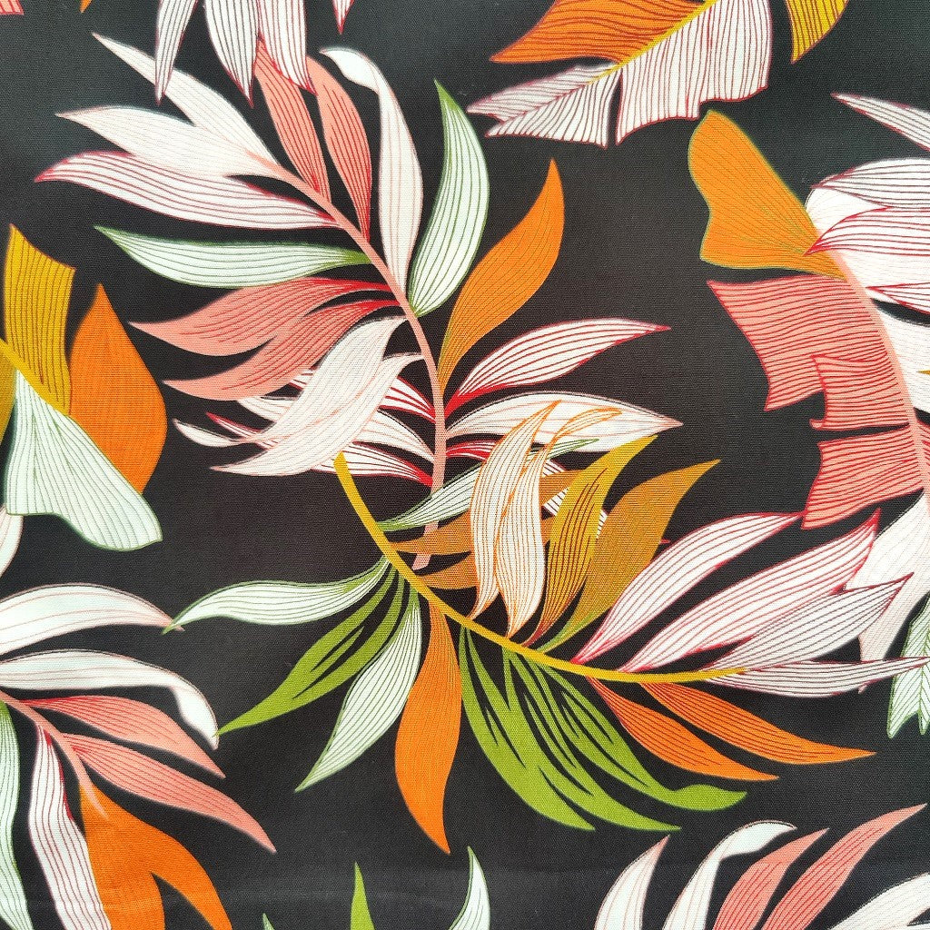 Tissu tahitien en coton, gros plan sur motifs feuilles de bananiers et fougères sur fond noir intense. Stock limité - aucun réassort.