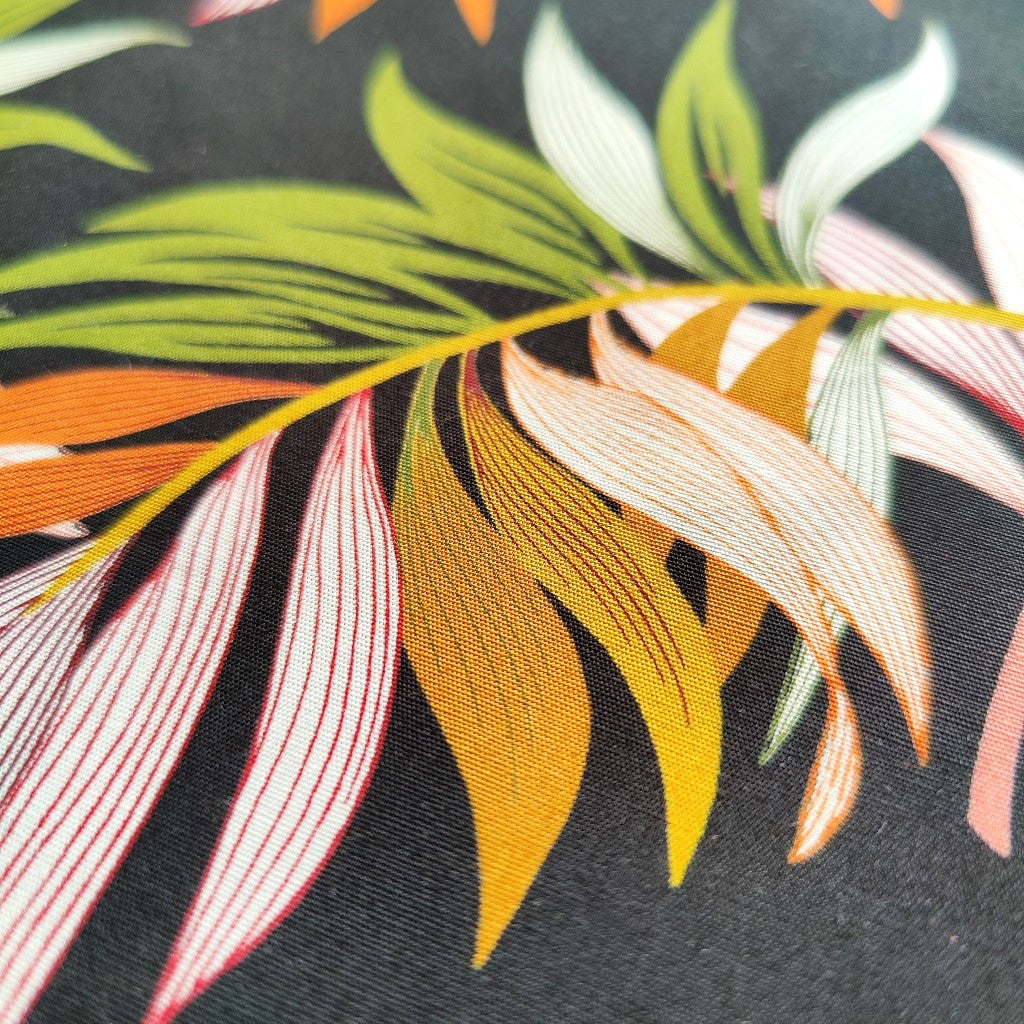 Tissu tahitien en coton, zoom sur motifs feuilles de bananiers et fougères vert et ocre sur fond noir intense. Idéal couture vêtement.